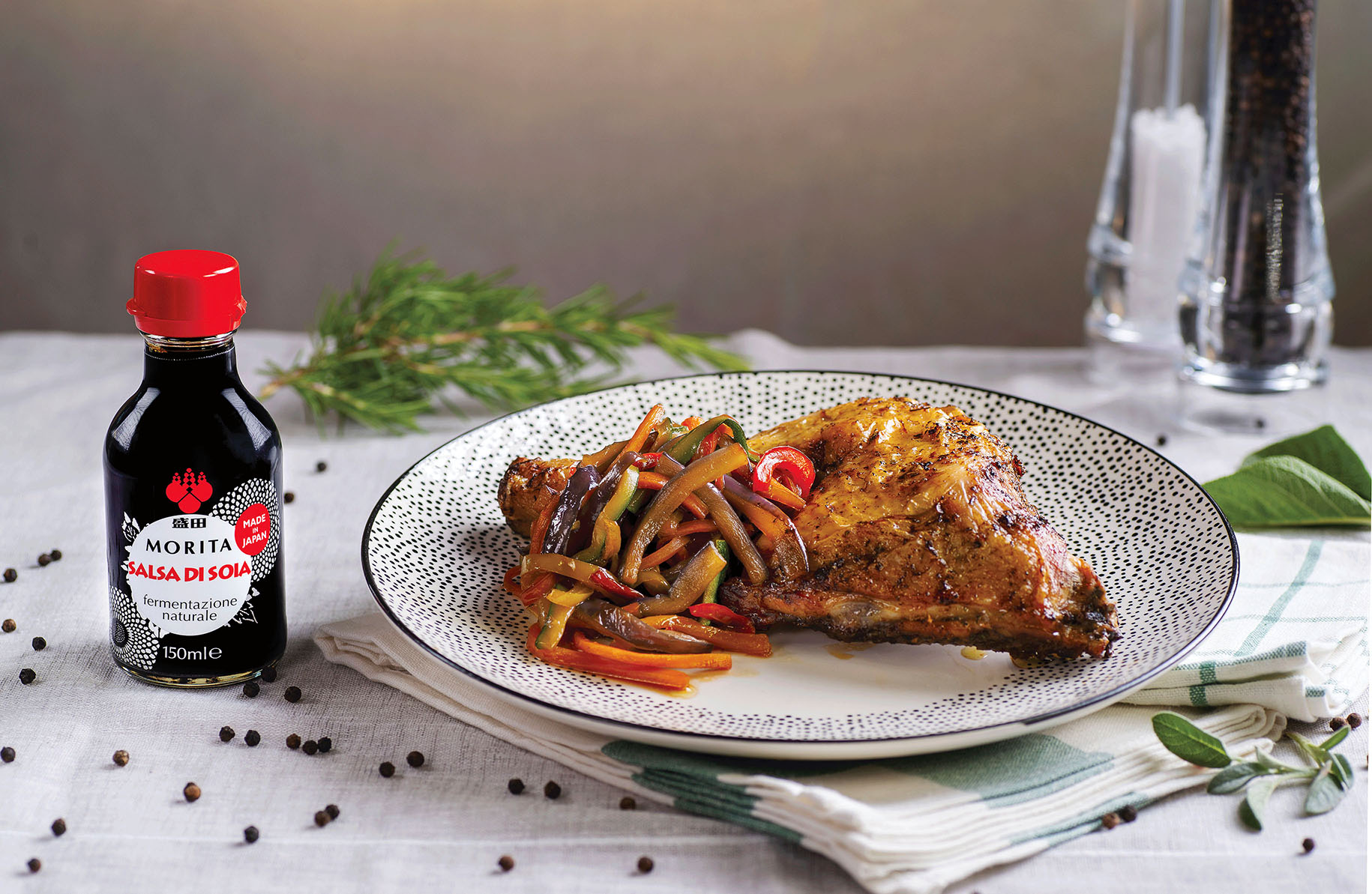 Un piatto di cosciotti di pollo marinati con le erbette accanto alla bottiglietta di salsa di soia Morita.
