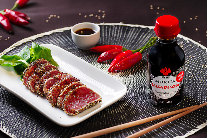 La boccetta di salsa di soia Morita tradizionale a lato di un piatto on tataki di tonno marinato.